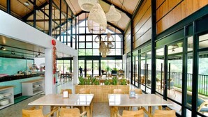 A spacious indoor area with large windows, wooden tables, and chairs. - Gulala Azana Hotel and Resort Guci Tegal (Songgom)