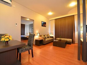 A hotel room with a dining area, a sofa set, a coffee table, and a large window with curtains. - Wixel Hotel Kendari (Kendari)