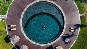 Vista aérea de una piscina circular con una persona nadando, rodeada por una terraza con sillas de descanso y sombrillas.