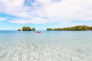 Un kayakista en un mar tranquilo con aguas transparentes y islas a lo lejos.