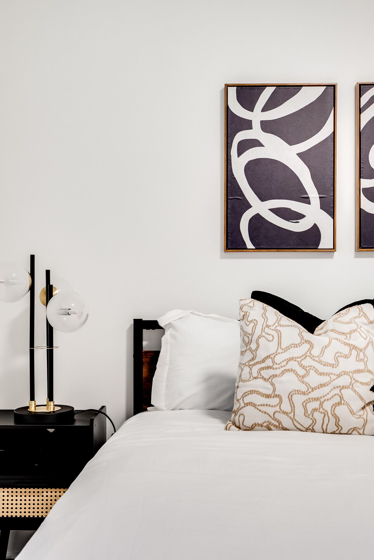 A neatly arranged bedroom with a bed, pillows, a bedside table with a lamp, and abstract artwork on the wall.