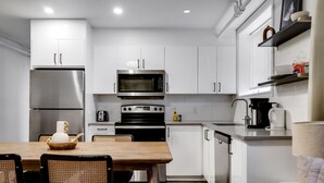 Cozinha moderna com armários brancos, eletrodomésticos de aço inoxidável, uma mesa de jantar com cadeiras e uma máquina de café.