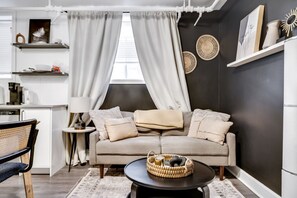 Una sala de estar moderna con sofá, mesa de centro y zona de comedor con una silla y una mesita.