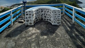 A stone bench with a curved backrest, a metal viewing platform, and a blue railing overlooking a coastal landscape. - Grande piscine, dans un environnement paisible, déconnexion totale assurée ! (la désirade)