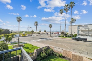 A street view with palm trees, a building with balconies, and a clear blue sky.