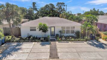 Una casa de un piso con puerta principal, un porche pequeño y un jardín con plantas variadas y una palmera.