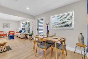 A modern living room with a dining area, featuring a sofa, chairs, a coffee table, and a dining table set for four. - Blue Lizard Men-Only 2-Bedroom 1-Bath Unit with Heated Saltwater Pool and Spa (Oakland Park)