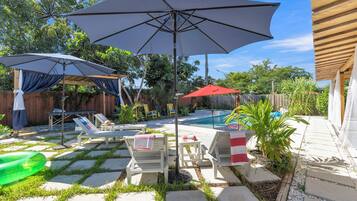 Un patio trasero con piscina, sillas de descanso y sombrillas.