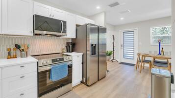 Una cocina moderna con armarios blancos, electrodomésticos de acero inoxidable y una zona de comedor con mesa y sillas de madera.