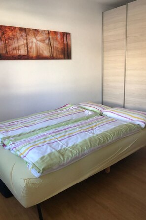 Una cama individual con colcha a rayas en una habitación con pared lisa y ventana con persianas.