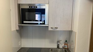 Eine kompakte Küche mit Backofen, Spüle aus Edelstahl und hellen Schränken.