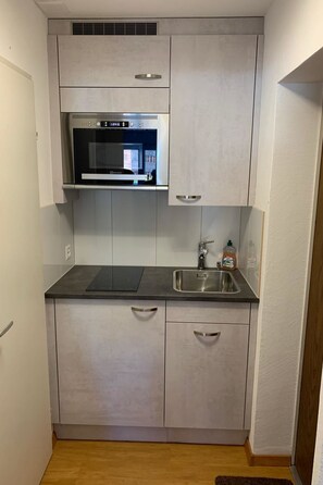 A compact kitchen with a built-in oven, a stainless steel sink, and light-colored cabinets. - Cristallina I, (Laax Uletsch), 37021 by Interhome (Laax)