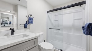 Une salle de bain moderne avec un lavabo, un miroir et des toilettes blancs, ainsi qu’un espace douche fermé par des parois de verre.