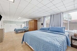 Ein Schlafzimmer mit einem großen Bett, zwei Einzelbetten, einem Kleiderschrank, einem Schreibtisch und einem Fenster mit Jalousien.