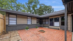 A residential building with a brick patio, wooden fence, and large windows.