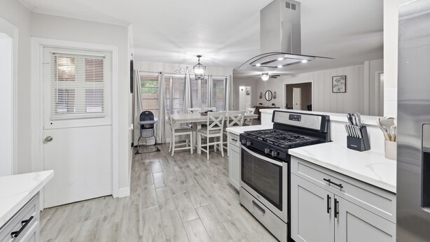 A modern kitchen with white cabinetry, a gas stove, and a stainless steel range hood.