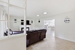 A modern living room with a brown leather sofa, a white entertainment unit, and a kitchen visible through an open doorway.