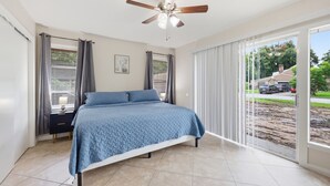 A bedroom with a bed, a ceiling fan, and a view of the outside.