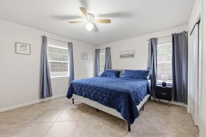 A bedroom with a bed, a ceiling fan, and two windows with curtains.