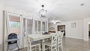 A dining area with a white table and chairs, a ceiling fan, and a chandelier.