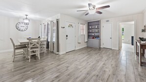 Une pièce spacieuse comprenant une table à manger, des chaises, un ventilateur de plafond et une horloge murale.