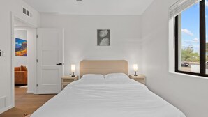 A bedroom with a bed, two bedside tables with lamps, a door leading to another room, and a window with a view. - Luxury 5 BR Retreat. Sleeps 10+. Near U of A. (Tucson)