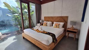 A hotel room with a bed, a nightstand, a lamp, and a view of a swimming pool. - LaVilla Duo Ubud - 2 Private Pool Villas (Gianyar)