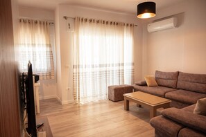 Ein modernes Wohnzimmer mit Sofa, Hocker und Fernseher.