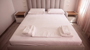 A neatly made bed with white linens and two towels folded at the foot. - Perla Apartment 02 in Plazhi San Pietro (Ishëm)