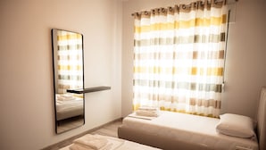 A hotel room with a bed, a bedside table, a mirror, and a window with striped curtains. - Perla Apartment 02 in Plazhi San Pietro (Ishëm)