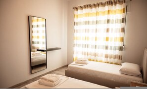 Ein Hotelzimmer mit einem Bett, einem Nachttisch, einem Spiegel und einem Fenster mit gestreiften Vorhängen.