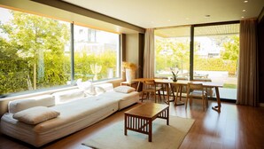 A modern living room with a sofa, wooden table, and chairs, large windows with a view of greenery. - Villa With Pool San Pietro Resort (Ishëm)