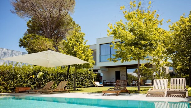 A swimming pool with lounge chairs and an umbrella, surrounded by trees and a modern building. - Villa With Pool San Pietro Resort (Ishëm)