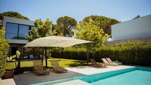 A swimming pool with lounge chairs and an umbrella, surrounded by a well-maintained garden and a modern building. - Villa With Pool San Pietro Resort (Ishëm)