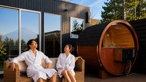A couple relaxing on a wicker sofa outside a modern building with large windows and a sauna. - Well Resort Fuji Annex (Gotemba)