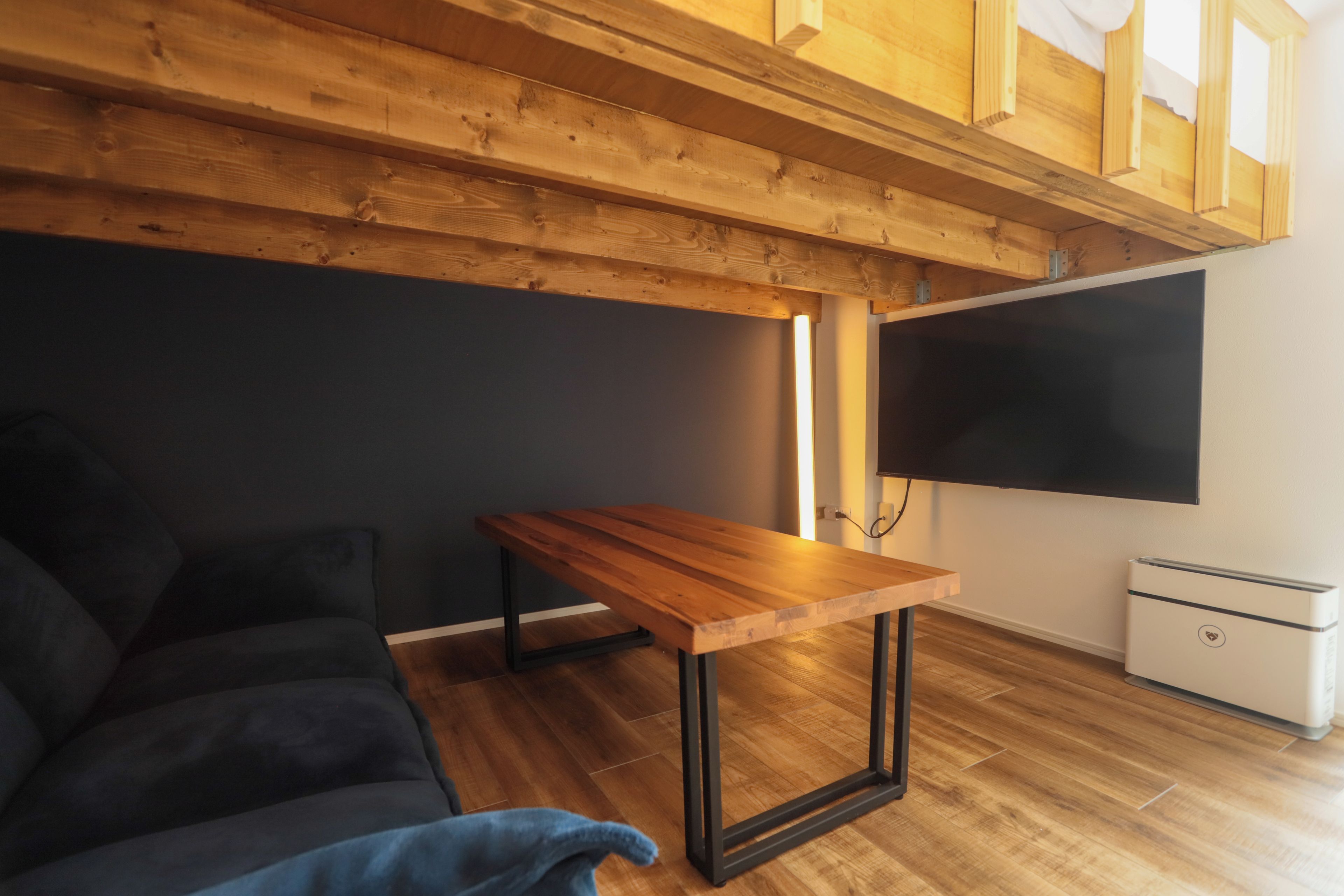 Una sala de estar moderna con techo de madera, un sofá negro, una mesa de centro de madera y un televisor de pantalla plana montado en la pared.