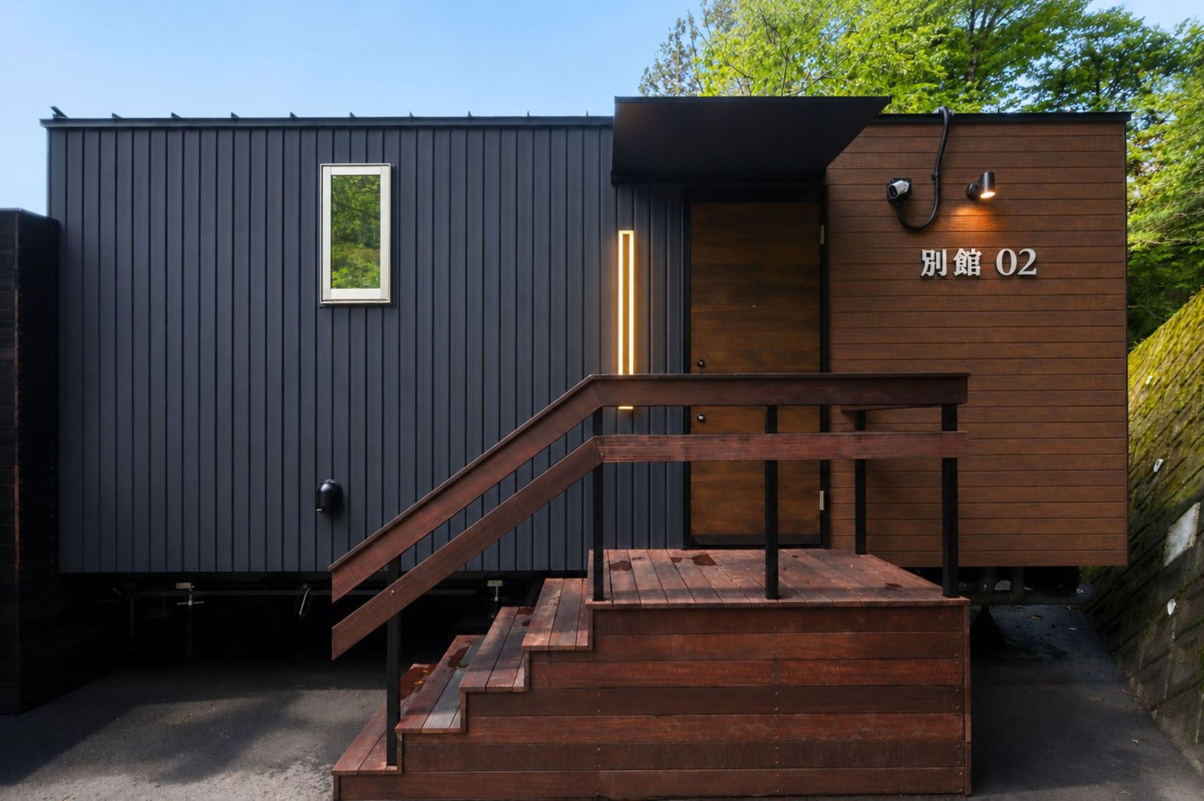 A modern building with a wooden staircase leading to a door marked '別館 02'.