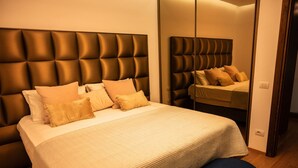 A bed with a tufted headboard, a bedside bench, and a mirror reflecting the bed. - Golden Pines Villa With Garden Perla Resort (Ishëm)