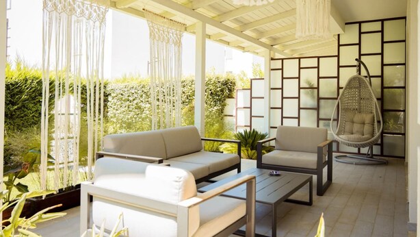 An outdoor patio with a sofa, chair, and hanging light fixture. - Golden Pines Villa With Garden Perla Resort (Ishëm)