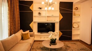 A living room with a sofa, a coffee table, a TV, and decorative shelves. - Golden Pines Villa With Garden Perla Resort (Ishëm)