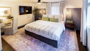 A modern bedroom with a large bed, a ceiling fan, a bedside table with a lamp, and a window with curtains. - One Block From Olde Town! Hot Tub, Fire Pit, Putting Green, Arcade & Game Room (Arvada)