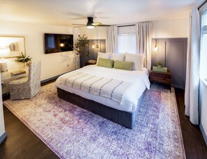 A modern bedroom with a large bed, a ceiling fan, a bedside table with a lamp, and a window with curtains. - One Block From Olde Town! Hot Tub, Fire Pit, Putting Green, Arcade & Game Room (Arvada)