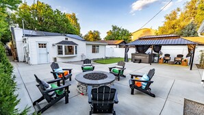 A backyard with a patio, outdoor seating, a fire pit, and a covered barbecue area. - One Block From Olde Town! Hot Tub, Fire Pit, Putting Green, Arcade & Game Room (Arvada)