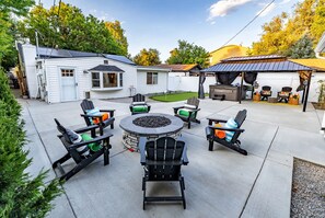 A backyard with a patio, outdoor seating, a fire pit, and a covered barbecue area. - One Block From Olde Town! Hot Tub, Fire Pit, Putting Green, Arcade & Game Room (Arvada)