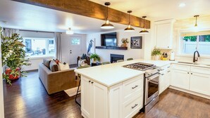 A modern kitchen with white cabinetry, a central island, and a dining area with a sofa. - One Block From Olde Town! Hot Tub, Fire Pit, Putting Green, Arcade & Game Room (Arvada)
