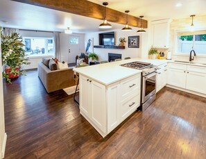 A modern kitchen with white cabinetry, a central island, and a dining area with a sofa. - One Block From Olde Town! Hot Tub, Fire Pit, Putting Green, Arcade & Game Room (Arvada)