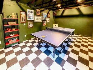 A ping pong table in a room with a checkered floor, green walls, and shelves with various items. - One Block From Olde Town! Hot Tub, Fire Pit, Putting Green, Arcade & Game Room (Arvada)