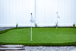 A well-maintained lawn with two white flags, a stone pathway, and a white building in the background. - One Block From Olde Town! Hot Tub, Fire Pit, Putting Green, Arcade & Game Room (Arvada)