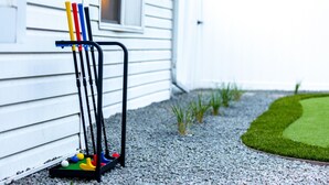 A golf cart with golf clubs and balls parked on a gravel surface next to a white building. - One Block From Olde Town! Hot Tub, Fire Pit, Putting Green, Arcade & Game Room (Arvada)