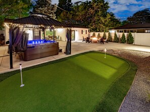 A backyard with a hot tub, patio furniture, and a well-maintained lawn. - One Block From Olde Town! Hot Tub, Fire Pit, Putting Green, Arcade & Game Room (Arvada)